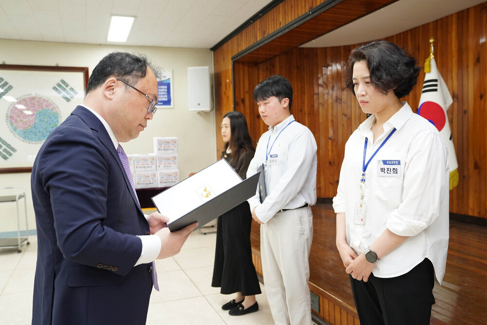 정장을 입고 안경을 낀 남성이 흰색 셔츠를 입은 박진희에게 상장을 수여하고 있다