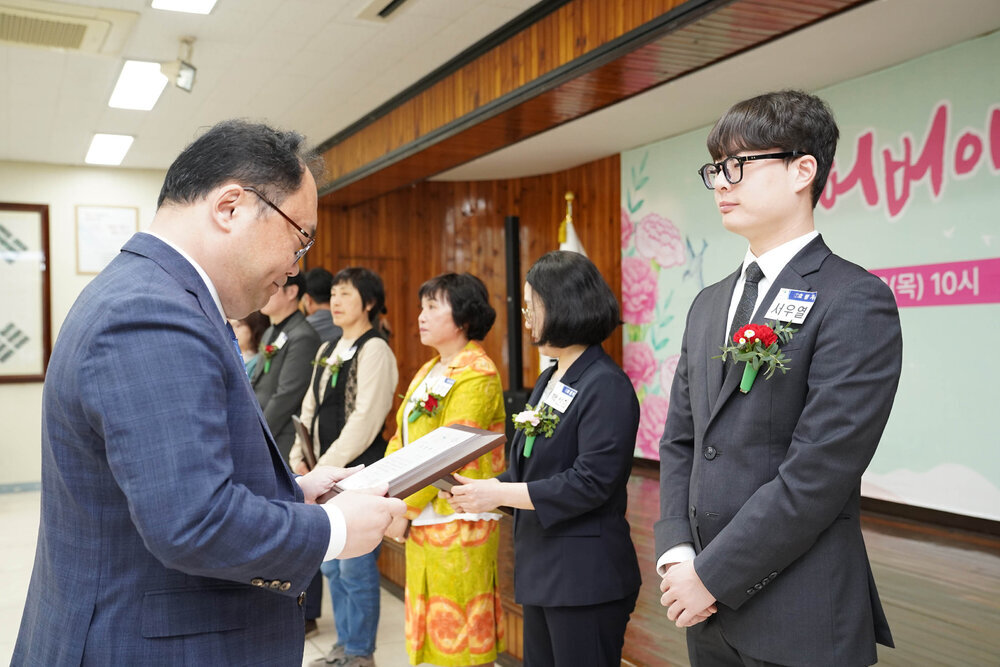 정장을 입고 안경을 낀 남성이 어두운 회색 정장을 입은 서우열에게 패를 수여하고 있다