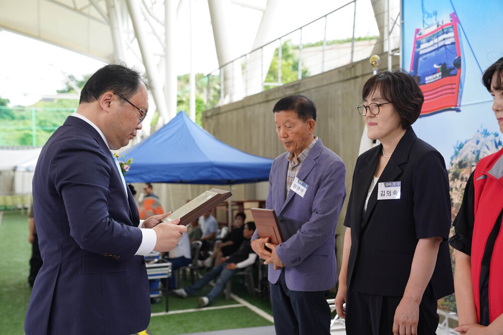 정장을 입고 안경을 낀 남성이 검은색 반팔 자켓을 입은 김희숙에게 패를 수여하고 있다