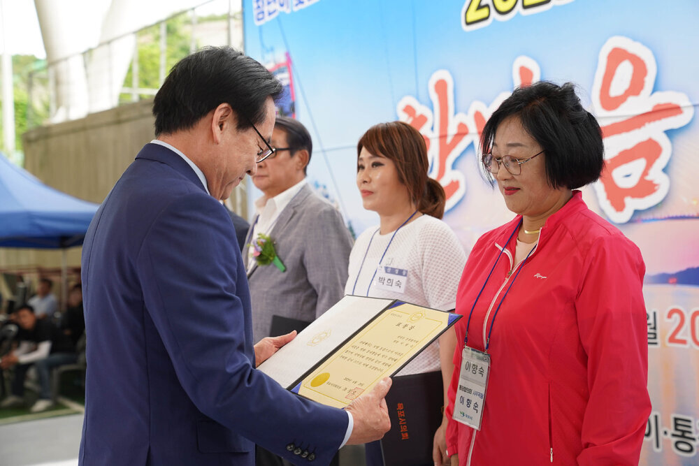 곤색 정장을 입고 안경을 낀 남성이 빨간색 바람막이를 입은 이향숙에게 상장을 수여하고 있다