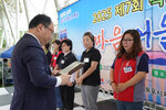 정장을 입고 안경을 낀 남성이 곤색 반팔티에 빨간색 작업조끼를 입은 문정미에게 패를 수여하고 있다