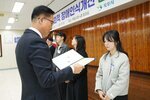 11월 정례조회로 정장을 입고 안경을 쓴 남성이 긴 곱슬머리를 반 뒤로 묵고서 밝은색 짧은 코트를 입은 조정선 수상자에게 상장을 수여 하고 있다.