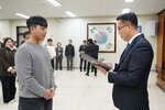 2026년 상반기 4급이하 정기인사로 정장을 입고 안경을 쓴 남성이 실내 행사장에서 한 남성에게 상장을 전달하며 내용을 읽고 있고, 남성은 회색 니트를 입고 두 손을 모은 채 서 있으며 뒤쪽에는 참석자들이 줄지어 서서 행사를 지켜보고 있다.